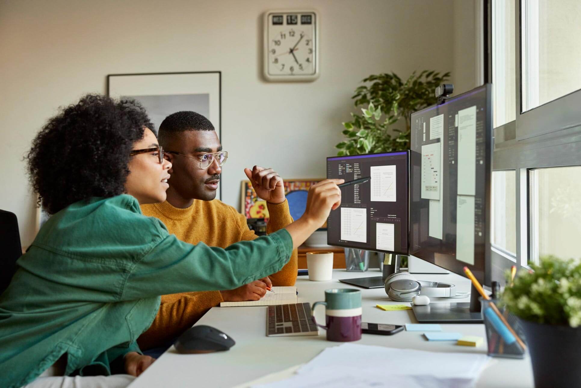 Two coworkers pointing at several computer monitors.